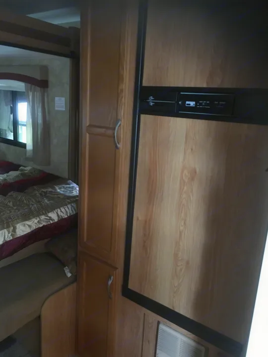 Inside an RV rental: wooden fridge, cabinets, and a peek into the compact bedroom with a window.. Jayco Jay Feather Ultra Lite 2012