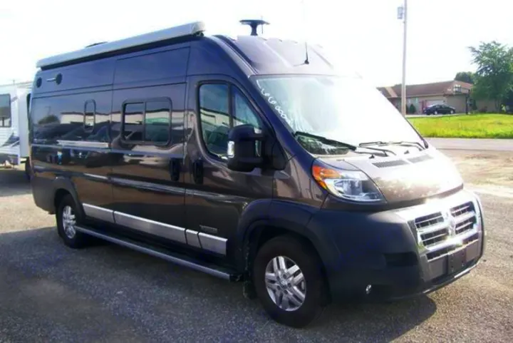 This dark grey Class B RV rental van with an awning is parked on gravel, ideal for travel adventures.. Winnebago Travato 2019