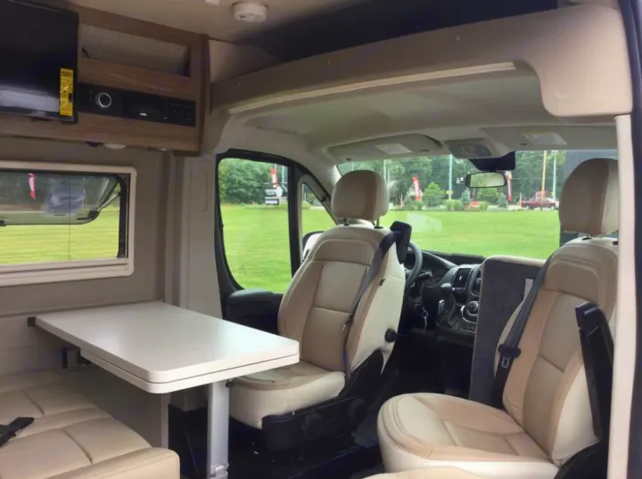 Inside an RV rental: swiveling front seats, dining table, and TV unit create a versatile camper van interior.. Winnebago Travato 2019
