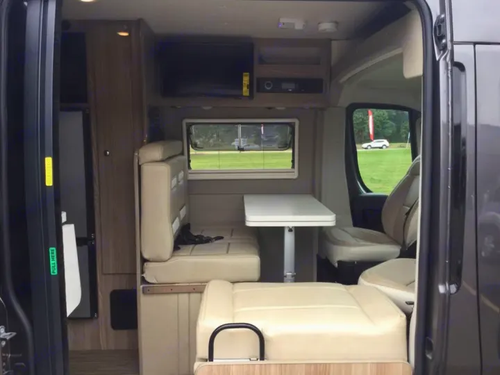This RV rental's camper van interior features a dinette, fridge, TV, and front seating, offering a compact living space.. Winnebago Travato 2019