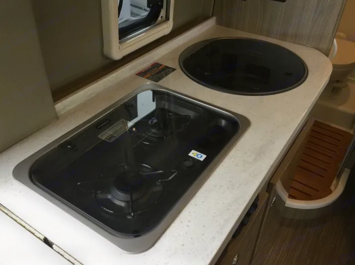 Compact RV rental kitchen with a two-burner stove, covered sink, and microwave, perfect for travel cooking.. Winnebago Travato 2019