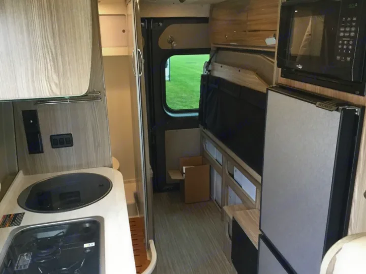 RV rental: Modern camper van interior with kitchen (sink/stovetop), microwave, fridge, and a convertible bed/seating area.. Winnebago Travato 2019