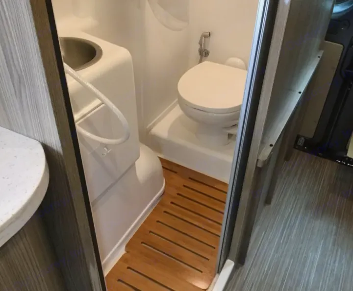 Explore this compact RV rental wet bath, featuring a toilet, integrated sink/shower, and wooden floor mat.. Winnebago Travato 2019