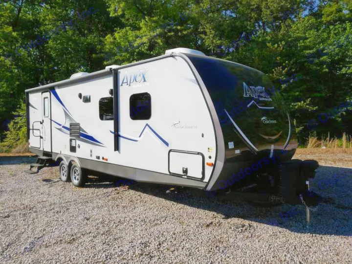 A grey and blue Coachmen Apex travel trailer, ready as an RV rental. This modern camper is parked on gravel, surrounded by trees.. Coachmen Apex 265rbss 2019