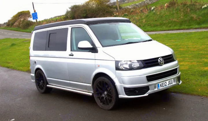 A silver Volkswagen campervan with pop-top, parked roadside. Ideal for RV rental adventures.. Volkswagen T5 premium camper 2012