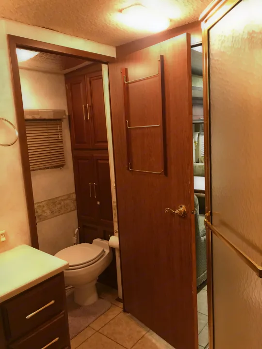 RV rental bathroom with a compact design, showing a toilet, wooden cabinets, and textured shower glass.. Winnebago Journey 2004