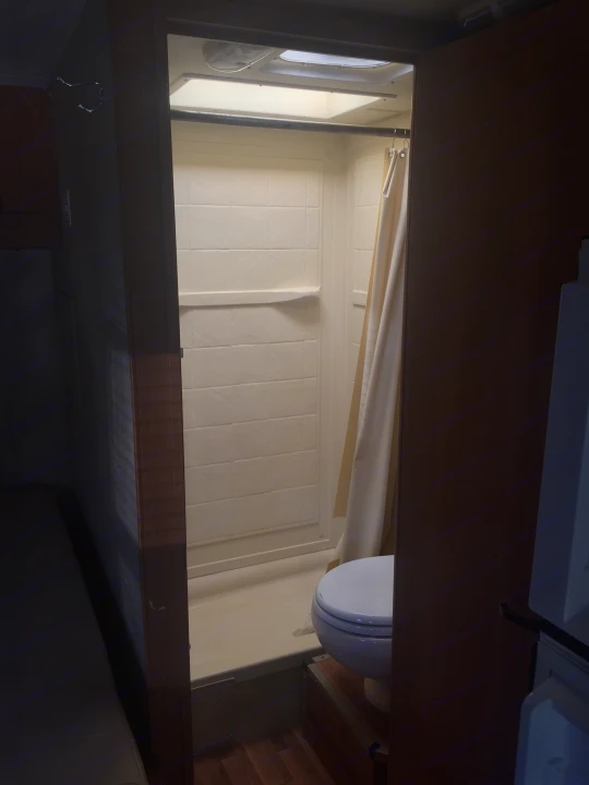 RV rental: Inside a compact RV bathroom, featuring a bright shower stall with a curtain and a white toilet.. Ford Majestic 23A 2012