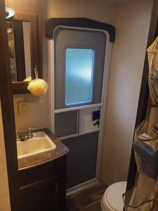 Compact RV rental bathroom with sink vanity, mirror, and door; includes a partially visible toilet and mesh storage.. Forest River Evo 2016