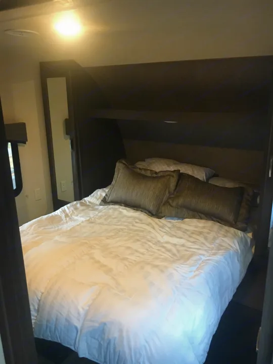 Comfortable RV rental bedroom featuring a cozy bed, built-in headboard with storage, and bright overhead lighting.. Forest River Evo 2016