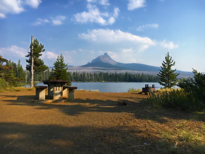 Scenic lakeside RV rental campsite with a concrete picnic table & fire pit. Features a striking mountain backdrop & unique forest.. Forest River Evo 2016