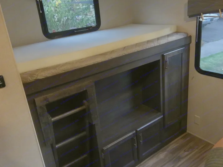 RV rental interior: A comfortable bunk bed with a thick foam topper sits above dark wood storage and shelving.. Forest River Evo 2016
