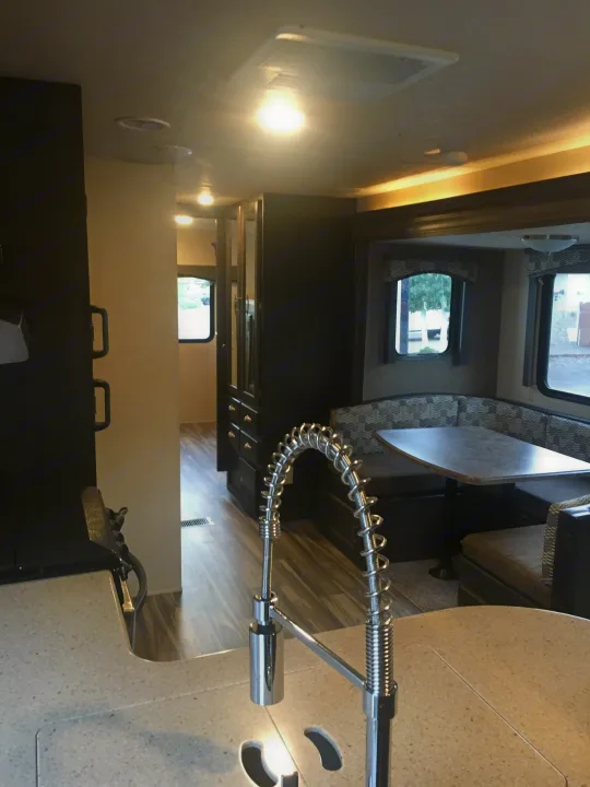 View inside an RV rental: a modern kitchen counter with a unique faucet leads to a cozy dining area with patterned seating and windows.. Forest River Evo 2016