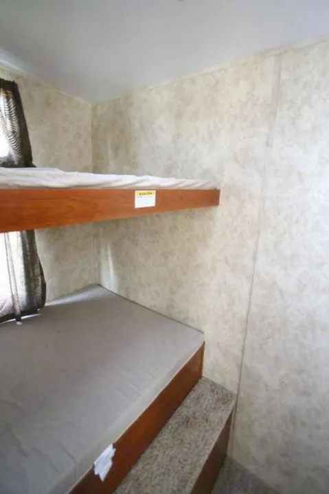RV rental bunk beds: a compact sleeping area featuring two mattresses, a window with curtains, and light textured walls.. Keystone Cougar 280BHS 2015