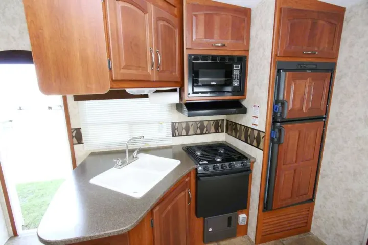 Compact RV rental kitchen with a double sink, stove, microwave, and a wood-paneled refrigerator, ready for your road trips.. Keystone Cougar 280BHS 2015