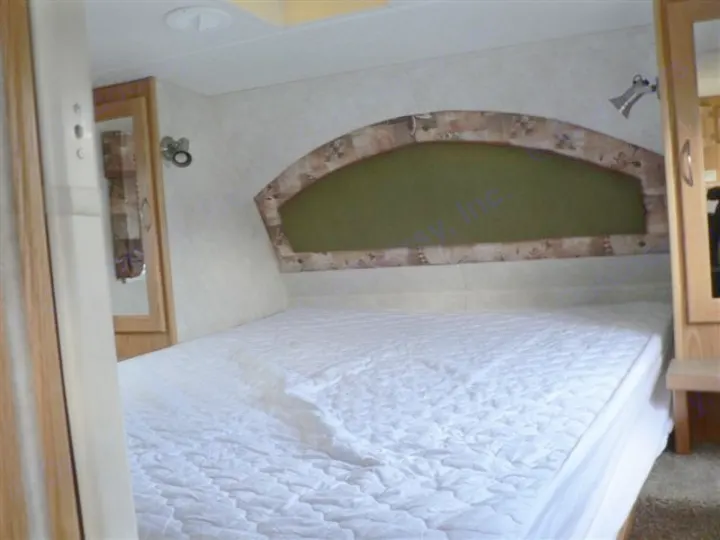 An rv rental interior bedroom features a clean, white-quilted bed and decorative arched headboard with reading lights.. Frontier FW255 2012