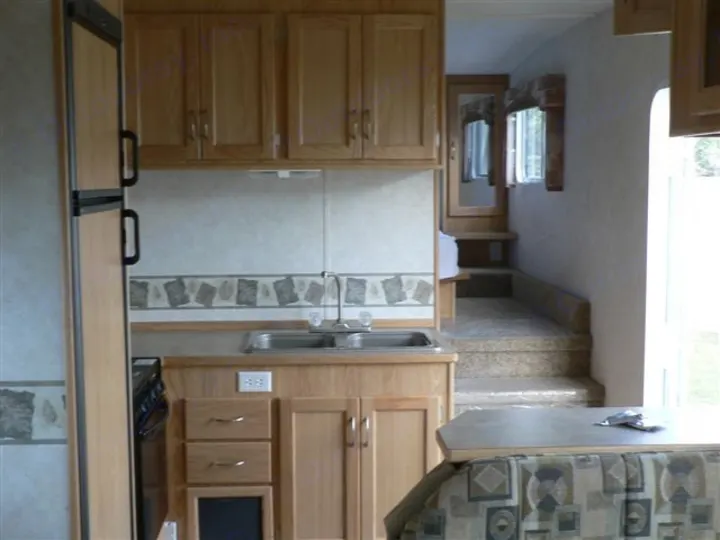 This RV rental interior features a compact kitchen with wood cabinets, double sink, fridge, dining booth, and steps.. Frontier FW255 2012