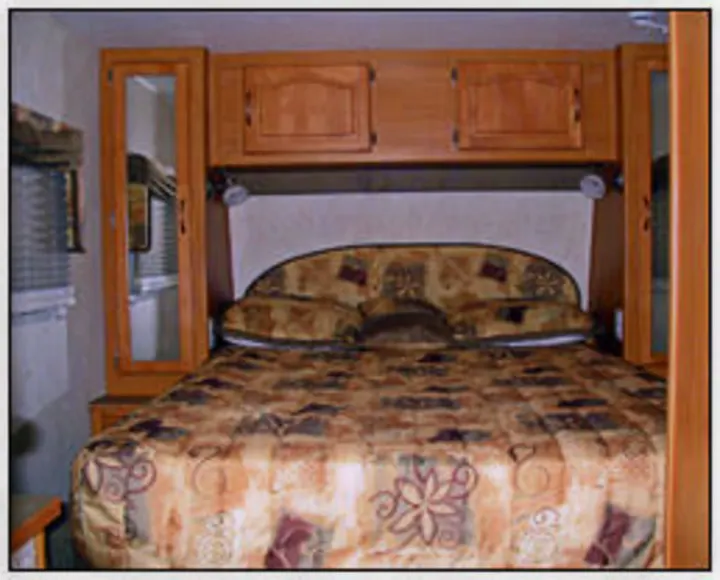 Cozy RV rental bedroom with a comfortable bed, patterned comforter, wood cabinets, and side mirrors. Perfect for travel.. Citation Supreme 29CKS 2012