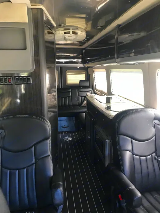 Luxurious RV rental interior: black leather captain's chairs, compact kitchen, rear lounge, and sleek design.. Airstream Interstate 2014