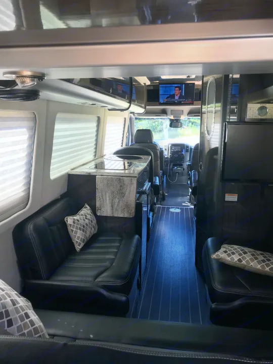 Luxurious RV rental interior with modern kitchenette, comfortable seating, and TV displaying news.. Airstream Interstate 2014