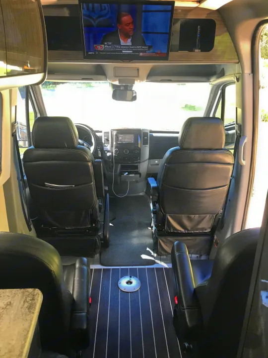 Spacious RV rental interior with swivel captain's chairs, front cockpit, & TV showing NFL. Ideal for mobile living & travel.. Airstream Interstate 2014
