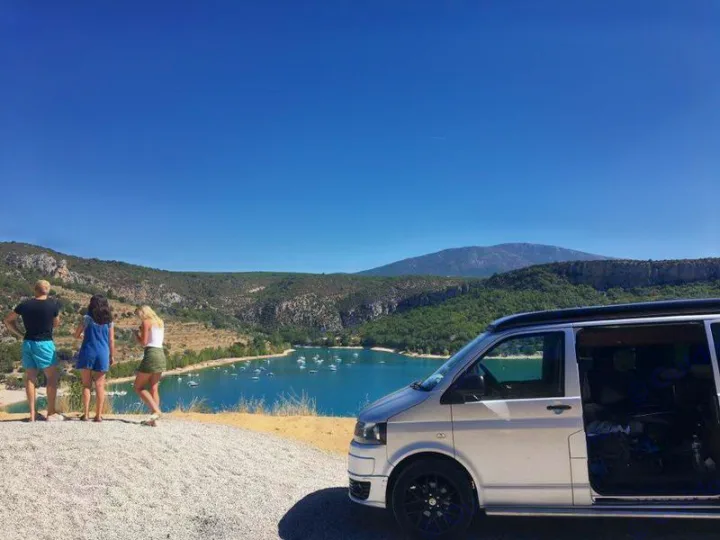 People admire the stunning lake and mountain view from their RV rental. A silver camper van is parked nearby under a clear sky.. Volkswagen T5 premium camper 2012