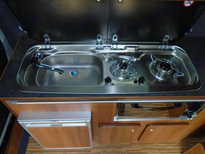 Integrated stainless steel sink, two-burner cooktop, and compact fridge in this RV rental kitchen.. Volkswagen T5 premium camper 2012