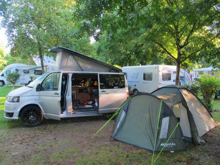 Camping site featuring a silver pop-top camper van (RV rental) with its door open, a green tent, and other caravans.. Volkswagen T5 premium camper 2012