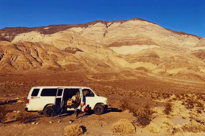 White RV rental in desert, huge mountains backdrop. Relaxing outside, perfect for your next adventure.. Ford E350 2000