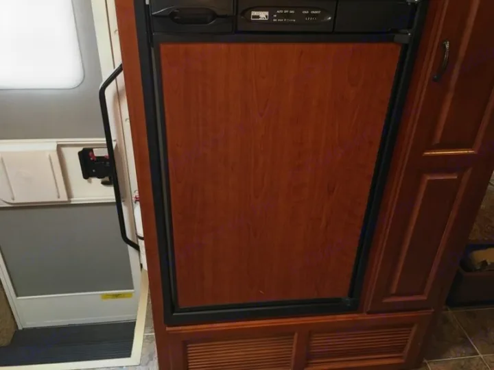 Inside an RV, a wood-paneled refrigerator with controls is next to the open entry door and grab handle. Perfect for rv rental.. Ford Hurricane 2011