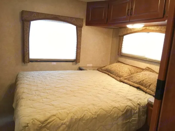 Cozy RV rental bedroom: Features a comfortable bed, two windows with shades, and overhead storage cabinets.. Ford Hurricane 2011