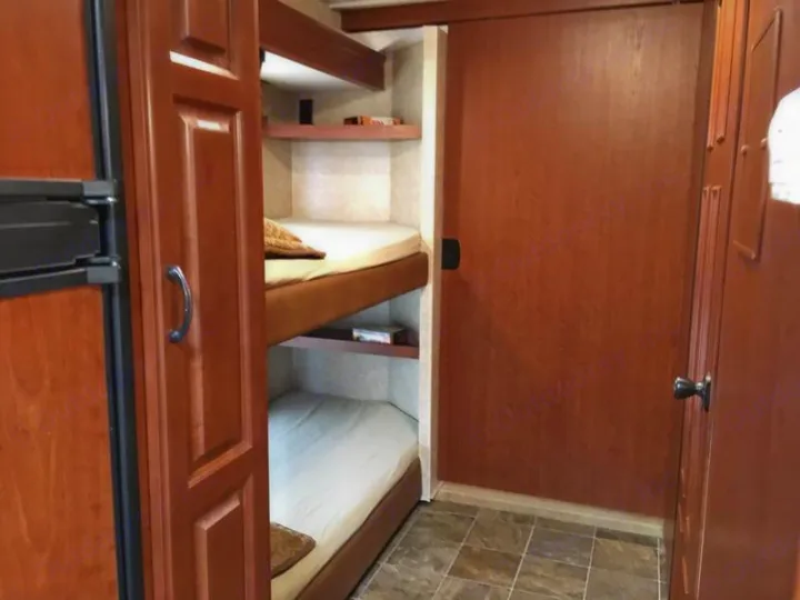 RV rental interior showing a refrigerator, two bunk beds with storage shelves, and a wooden sliding door.. Ford Hurricane 2011