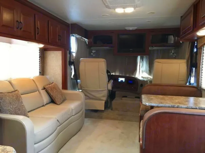 Spacious RV rental interior featuring a cream sofa, driver/passenger seats, dining booth, overhead cabinets, and TV.. Ford Hurricane 2011