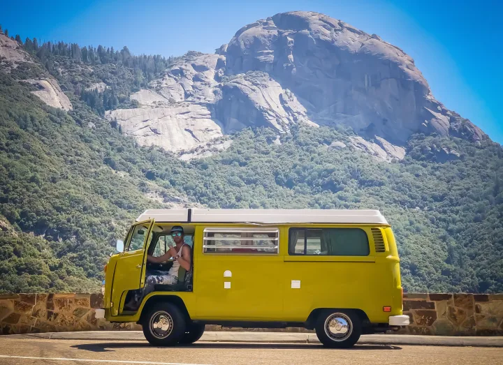 Enjoying a vintage RV rental adventure, a man in a yellow camper van poses against a grand mountain backdrop.. Volkswagen Westfalia 1977