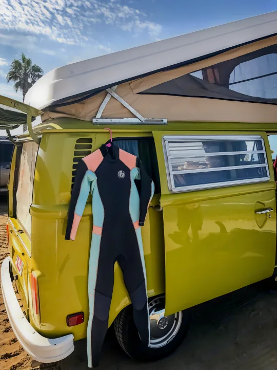 Vintage yellow VW camper van with pop-top and hanging wetsuit on a sunny beach. Ideal RV rental for surfing adventures.. Volkswagen Westfalia 1977