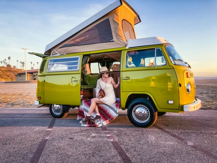 An RV rental motorhome with bike rack and tent on green grass at a campsite under a partly cloudy sky.. Volkswagen Westfalia 1977