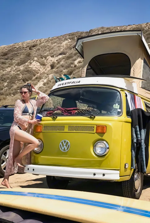 Coastal adventure awaits! A woman poses with a classic yellow VW Westfalia pop-top camper van, ideal for RV rental fun.. Volkswagen Westfalia 1977