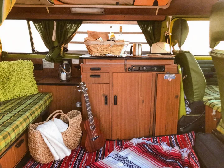 Inside a classic Westfalia RV rental, featuring a cozy kitchenette, ukulele, and picnic setup for travel.. Volkswagen Westfalia 1977