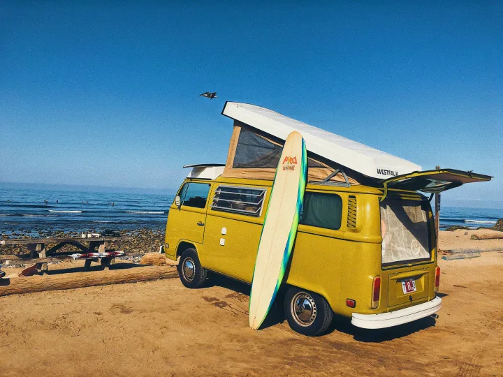 This yellow pop-top VW Westfalia RV rental is parked beachside with a surfboard, ready for ocean adventures.. Volkswagen Westfalia 1977