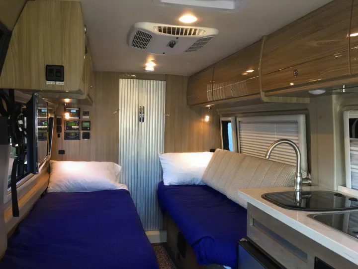 Cozy RV rental interior featuring twin beds, compact kitchen, and overhead storage, ideal for mobile living.. Winnebago Travato 59K 2019