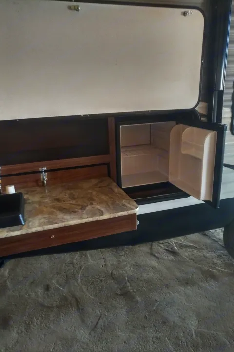 Outdoor kitchen setup in an RV rental, featuring a sink, faucet, and open mini-fridge. Ready for adventures!. Coleman 244BH 2017