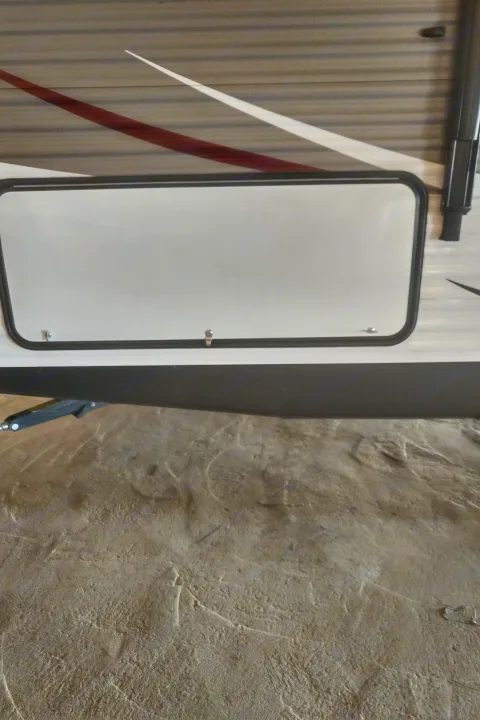 Side of an RV rental: white exterior storage door with black trim, striped decals, and ground. See key camper features.. Coleman 244BH 2017