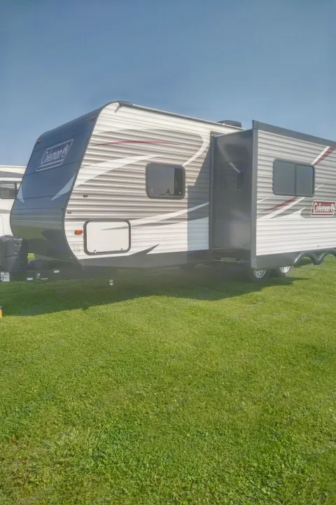 Coleman travel trailer for RV rental, showing extended slide-out on green grass under a clear blue sky.. Coleman 244BH 2017