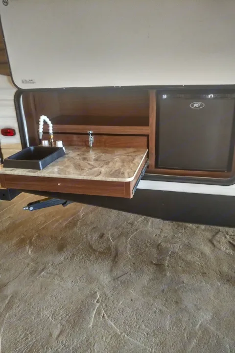 Explore this RV rental's outdoor kitchen featuring a slide-out counter, sink, and mini-fridge for camping convenience.. Coleman 244BH 2017