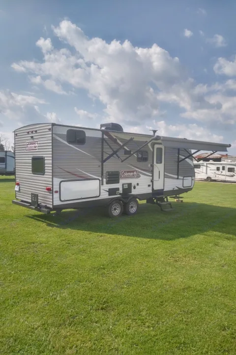 This Coleman travel trailer, an RV rental, is shown parked on green grass with its awning extended under a cloudy sky.. Coleman 244BH 2017