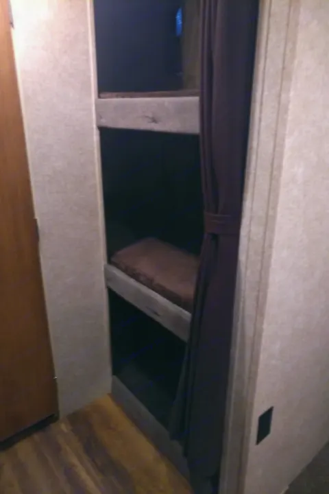 Compact RV rental bunk beds. Cozy sleeping area in a travel trailer interior, with wood floors & a privacy curtain.. Catalina 221TBS 2018