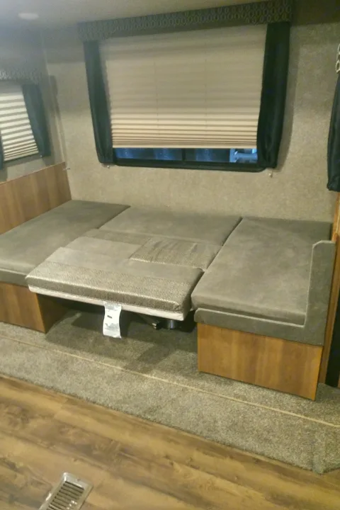 Inside an **RV rental**, a grey convertible dinette transforms into a bed, featuring wood trim and mixed flooring.. Catalina 221TBS 2018