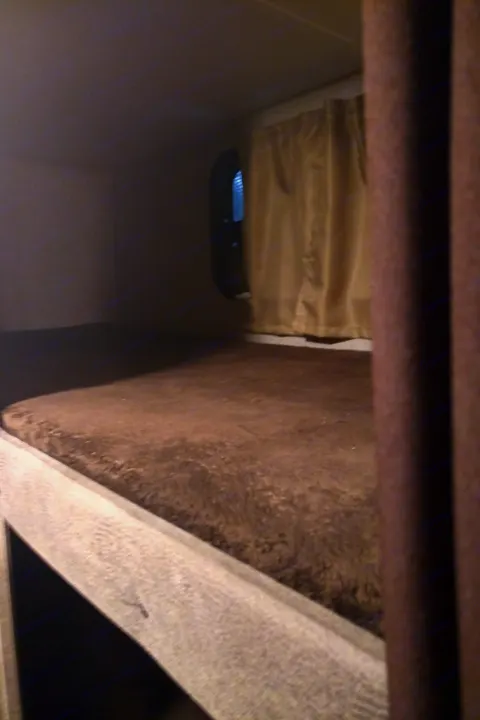 Cozy RV rental bunk bed features a soft brown mattress and window with a light-blocking curtain, ideal for travel.. Catalina 221TBS 2018