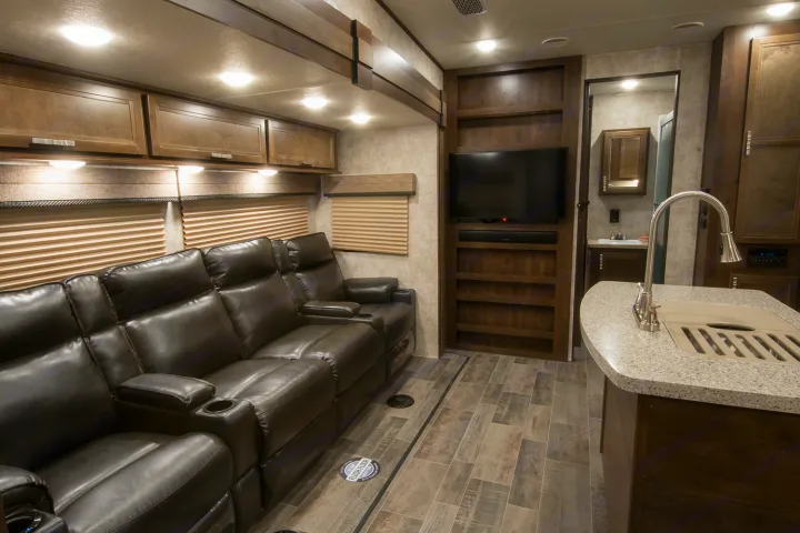 Luxury rv rental interior: dark leather reclining sofa, large TV, built-in shelves, and kitchen island with sink.. Highland Ridge RV Highlander Toy Hauler 2019