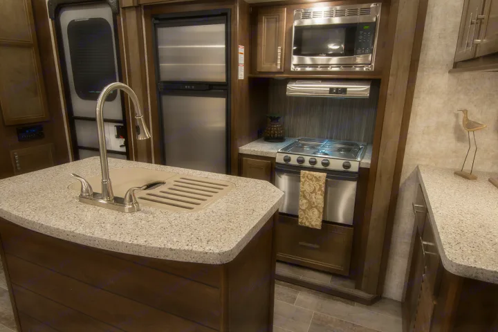 Modern RV rental kitchen with island sink, stainless appliances, and warm wood tones. Perfect for your road trip!. Highland Ridge RV Highlander Toy Hauler 2019