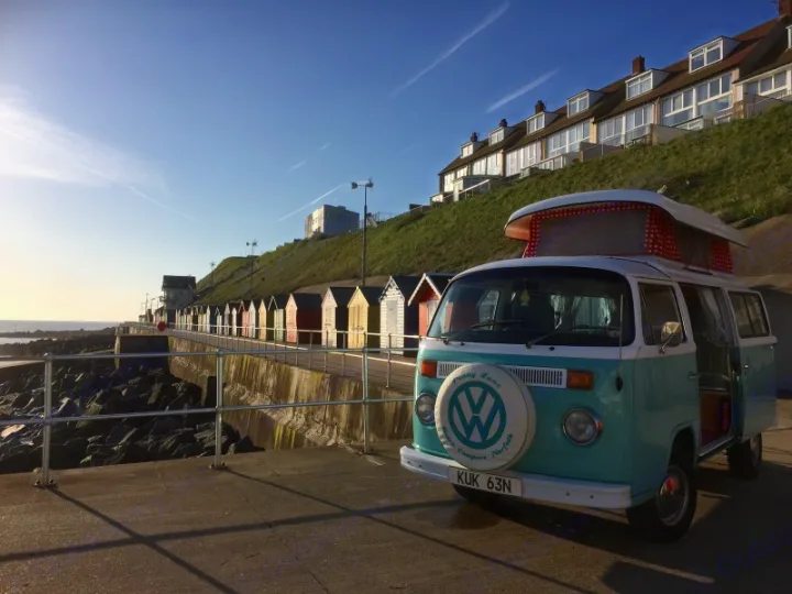 Coastal RV rental: A classic blue VW campervan by colorful beach huts & sea.. Volkswagen 2.0L T2 Late Bay 1975